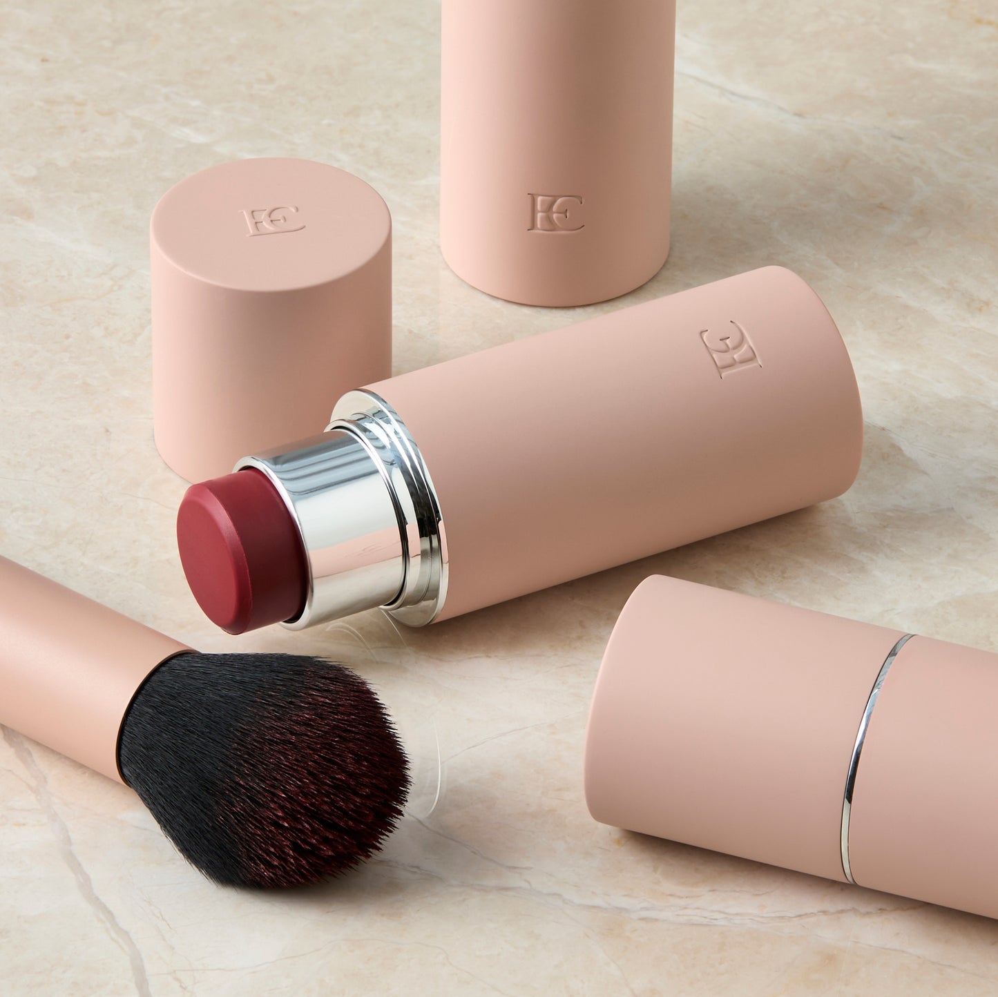 DEEPCHERRYBLUSH-1 Makeup products including a lipstick, brush, and two containers on a light surface.