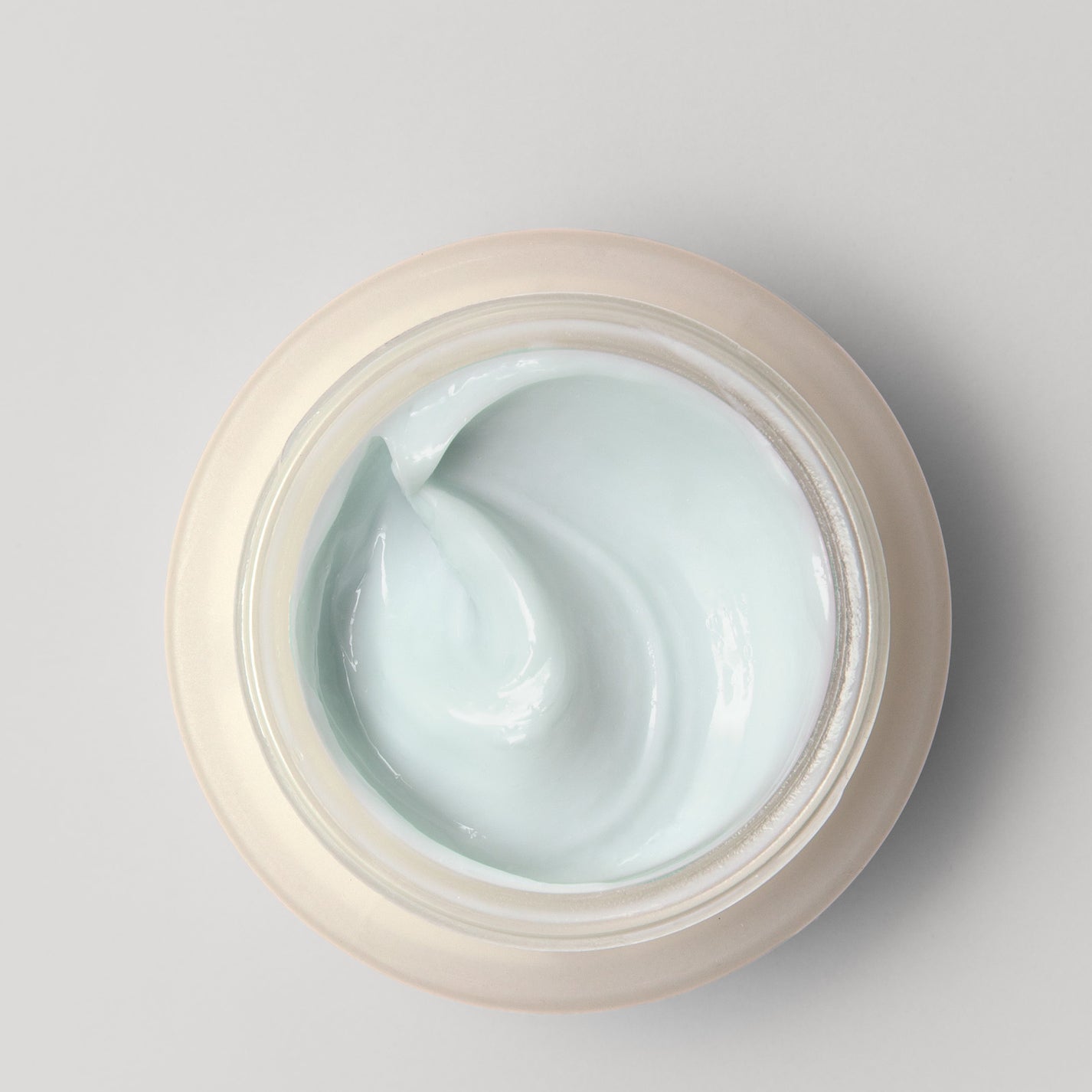 An open jar of light blue cream against a neutral background.